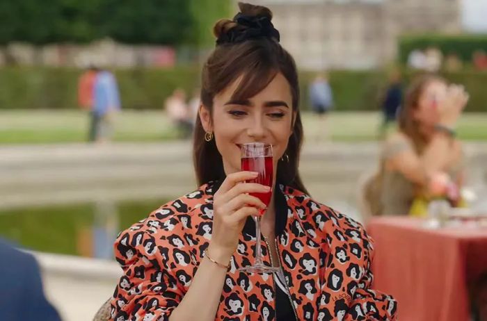 A screenshot of Emily sipping a Kir Royale cocktail from *Emily in Paris* on Netflix.