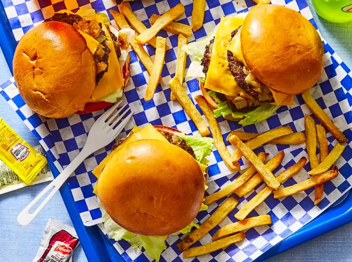 A top-down view of three cheeseburgers on a checkered tablecloth, accompanied by a side of fries.