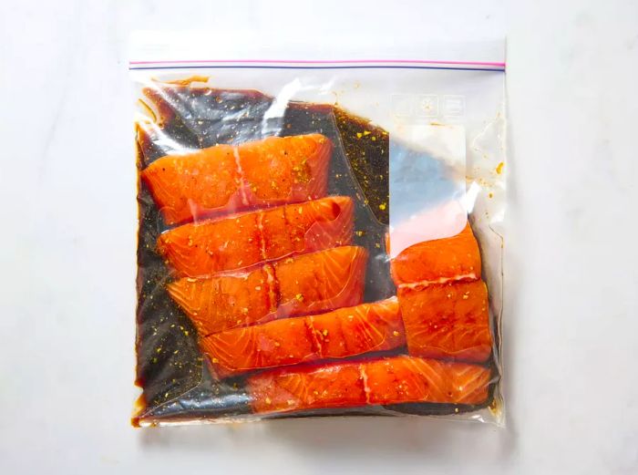 A resealable plastic bag containing salmon fillets soaking in marinade.