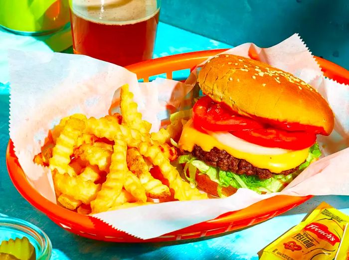 A delicious smash burger cheeseburger served in a classic fast food basket, complete with crinkle-cut fries and a side of yellow mustard packets.