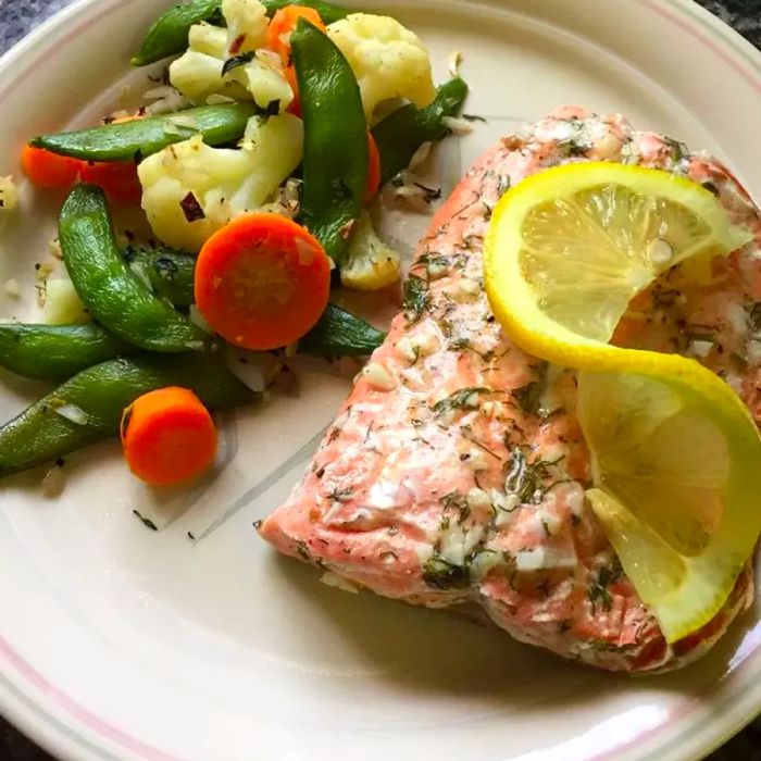 Salmon garnished with dill and lemon, served with a side of vegetables