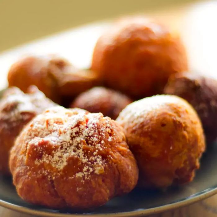 Close-up of jelly doughnuts, lightly dusted with powdered sugar, on a dark-glazed ceramic plate