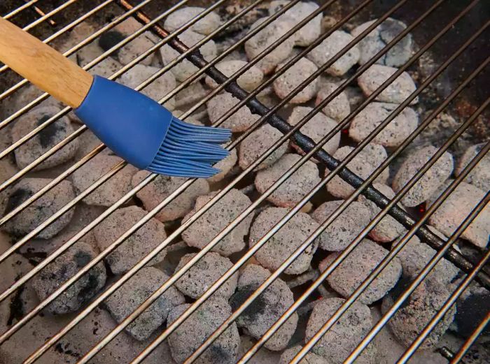 A pastry brush applying oil to the grill grates.