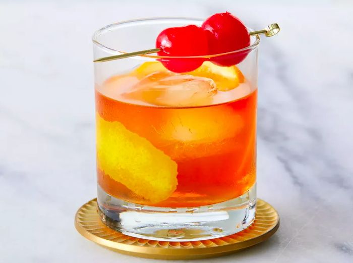 Close-up shot of an Old Fashioned cocktail, garnished with maraschino cherries.