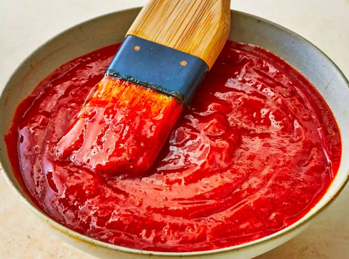 A close-up of barbecue sauce with a brush resting in the sauce.