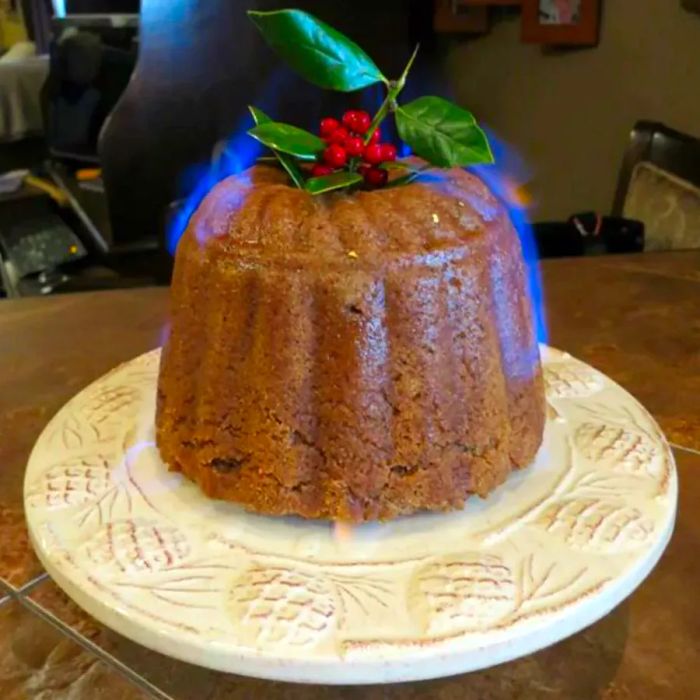 A steamed plum pudding lit with blue flames, topped with a sprig of holly