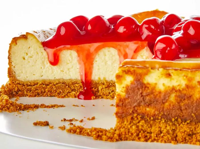 A low-angle shot of a cheesecake with a few slices missing, topped with juicy cherries.