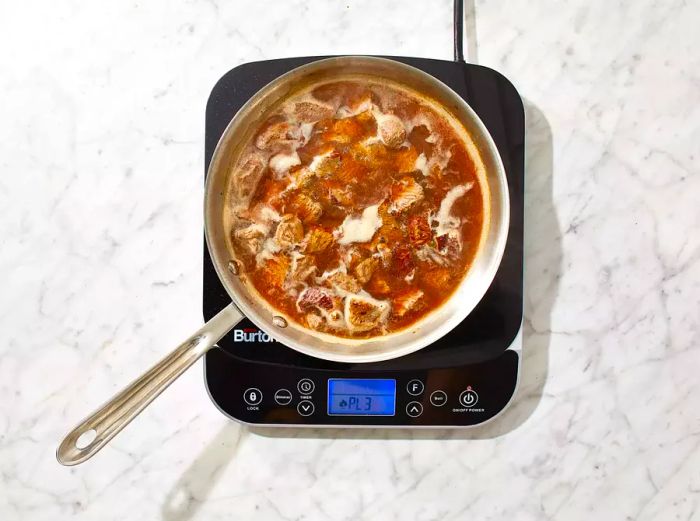 Beef browning in a pan, with water added and simmering for a few hours until the meat easily shreds.