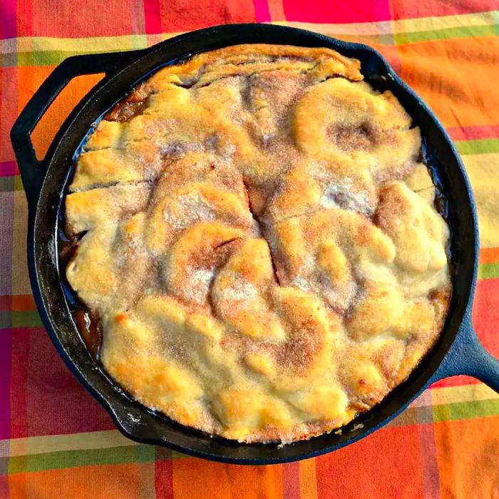 a top-down shot of a golden-brown apple pie with a flaky crust in a cast iron skillet