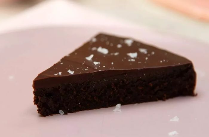 A slice of decadently rich cake topped with glossy ganache and a sprinkle of flaky sea salt.