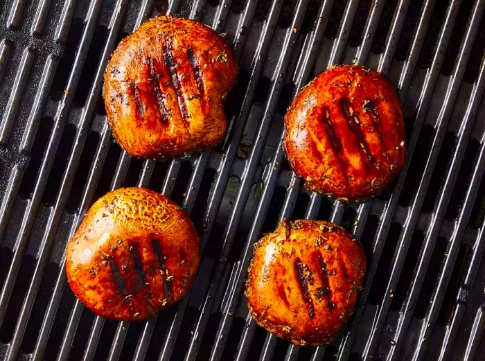 Four grilled portobello mushroom caps resting on the grill grates.