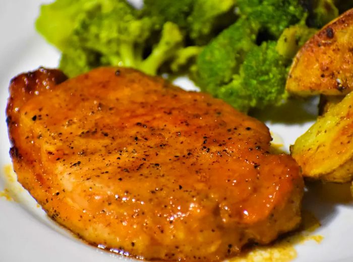 A close-up shot of a Honey-Garlic Pork Chop served alongside broccoli on a plate.