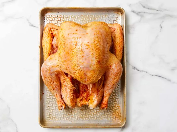 A whole, raw turkey coated with Creole seasoning, resting on a baking sheet.