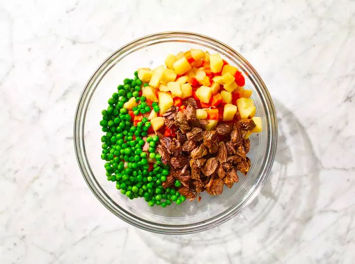 Carrots, potatoes, and peas are added to the mixing bowl with the beef.