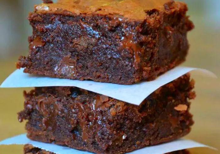 A batch of gooey brownies stacked with parchment paper between them.