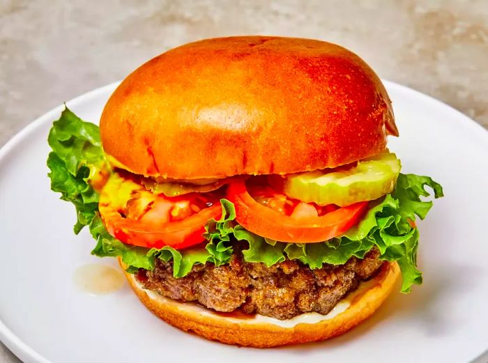 A close-up view showcasing the juicy layers of a hamburger, topped with crisp lettuce, fresh tomatoes, and tangy pickles.