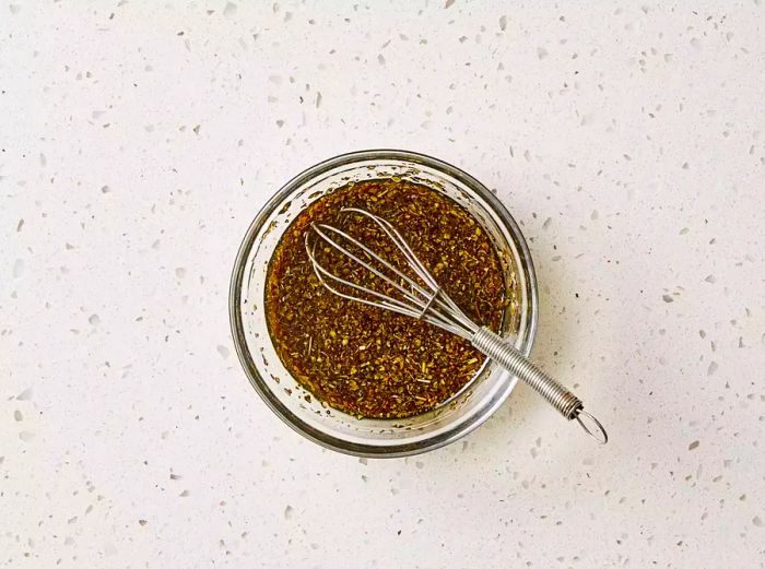 A small bowl filled with seasoned vinaigrette, accompanied by a whisk.