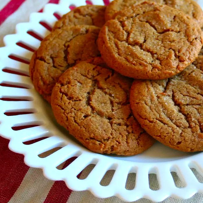 A white plate with a delicate scalloped edge, showcasing molasses ginger cookies dusted with sugar