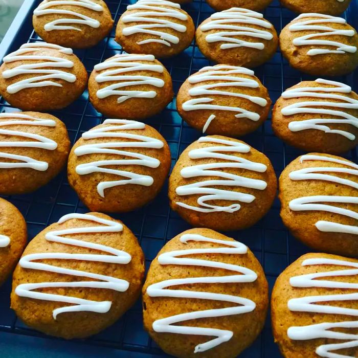 Pumpkin cookies drizzled with white zigzag icing, cooling on a wire rack