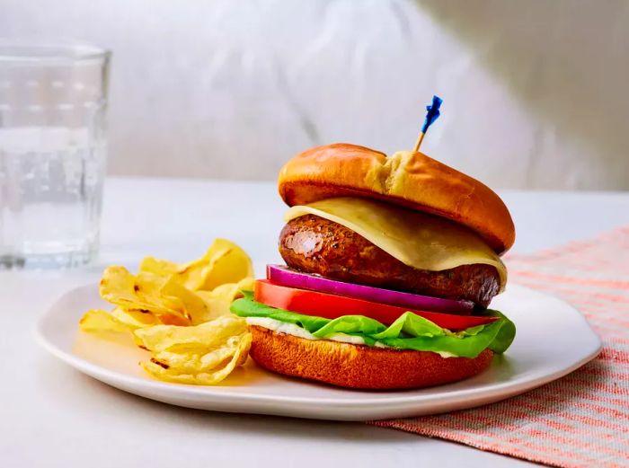 A portobello mushroom burger topped with cheese, lettuce, tomato, and onion, served alongside potato chips.