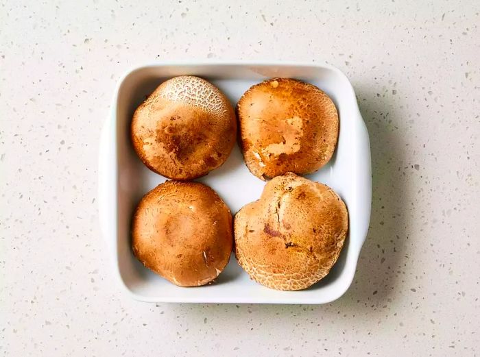 A shallow dish containing four portobello mushroom caps.