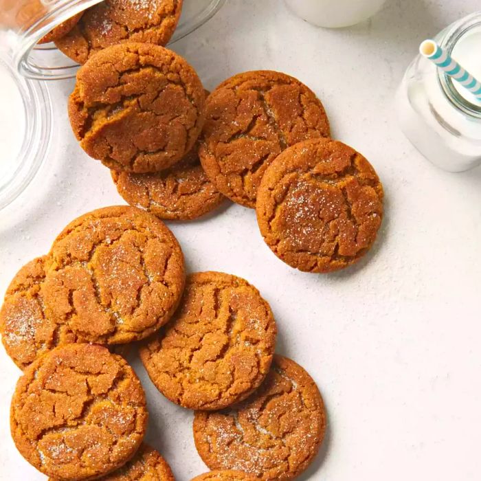 An overhead shot of Grandma's Gingersnap Cookies tumbling out of a glass cookie jar and onto a countertop