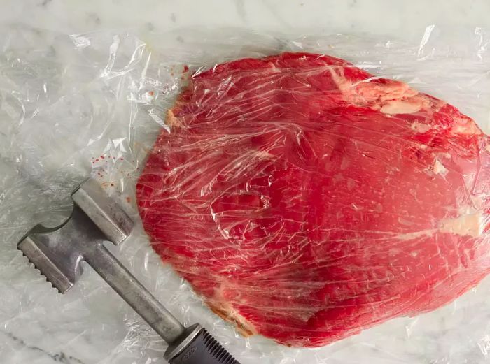 Pound the steak between two sheets of plastic, using the smooth side of a meat mallet.