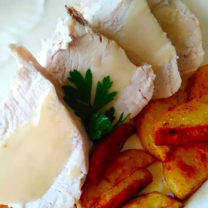 close-up of turkey breast slices topped with gravy, accompanied by roasted potatoes