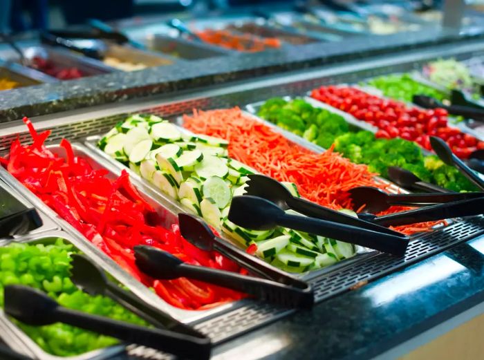 A salad bar filled with fresh veggies and utensils