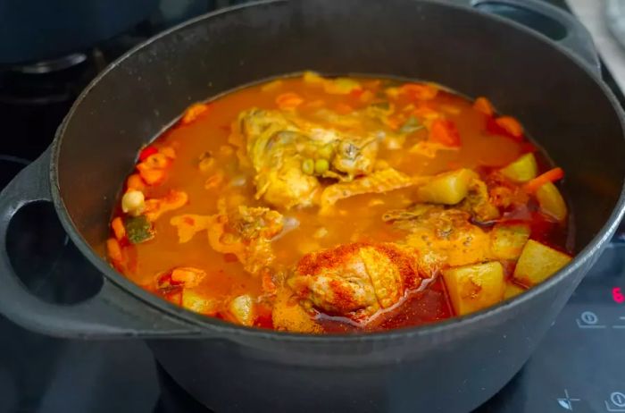 Chicken thighs simmering in a spicy broth with Mediterranean vegetables.