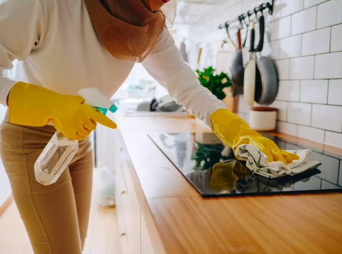 A Muslim woman cleaning the cooking panel on a kitchen cooktop.