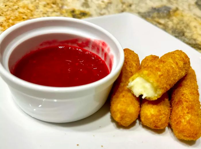 A plate of mozzarella sticks with raspberry Melba sauce on the side