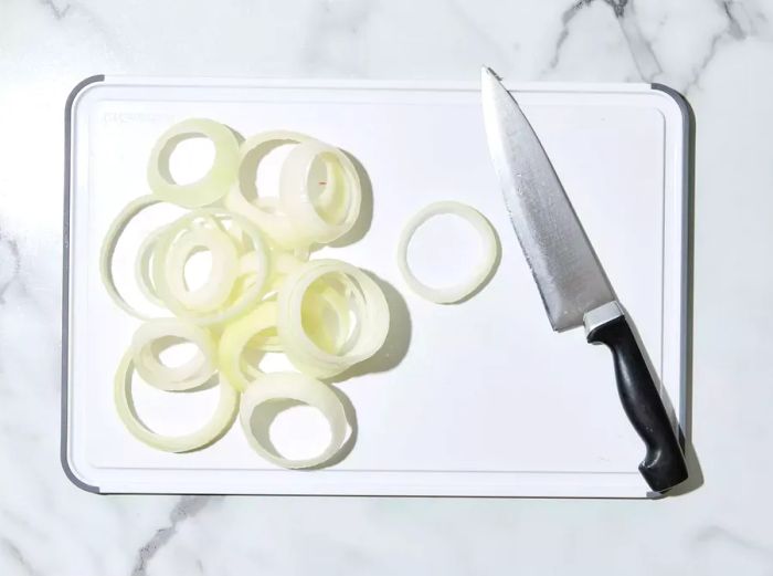 A cutting board with onion rings sliced and a knife