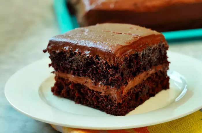 Close-up of a slice of One Bowl Chocolate Cake, transformed into a layered sheet cake with rich chocolate frosting.