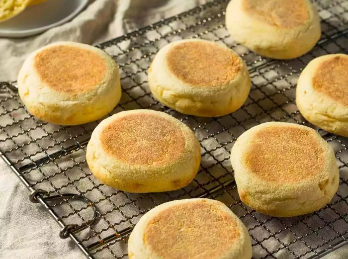 English muffins resting on a cooling rack with a linen cloth beneath