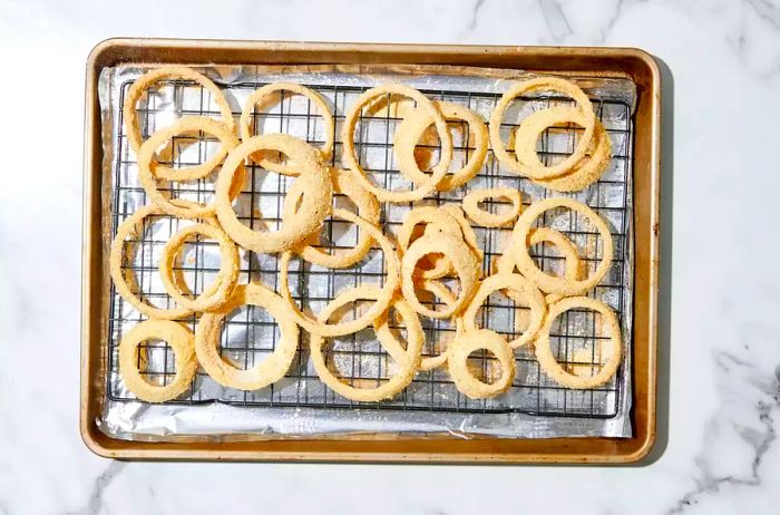 A foil-lined baking sheet with a metal rack, holding onion slices coated in breadcrumbs