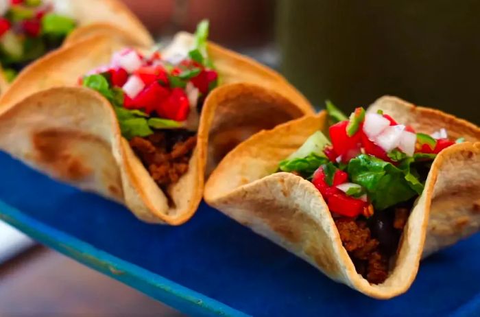 Homemade tortilla bowls filled with seasoned ground beef, lettuce, tomatoes, and onions.