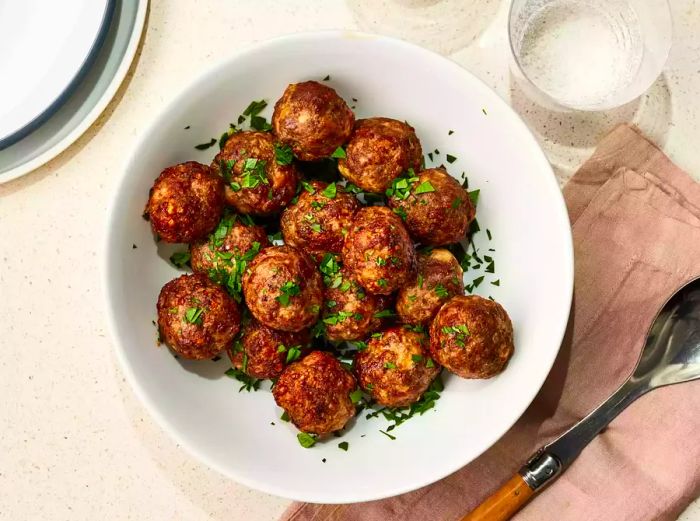 A top-down shot of a bowl filled with air fryer meatballs, topped with freshly chopped parsley.