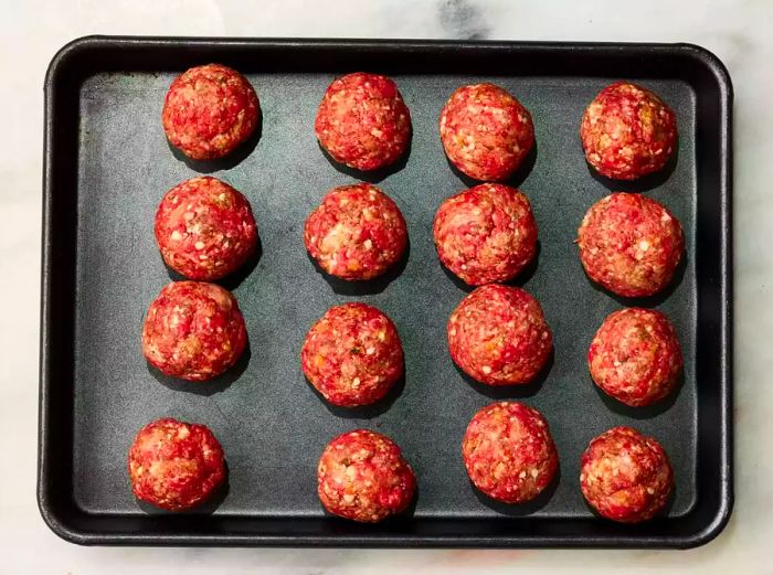 12 meatballs shaped and arranged on a baking tray.