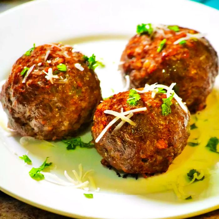 A close-up shot of Italian baked meatballs with cheese and herbs on a plate.