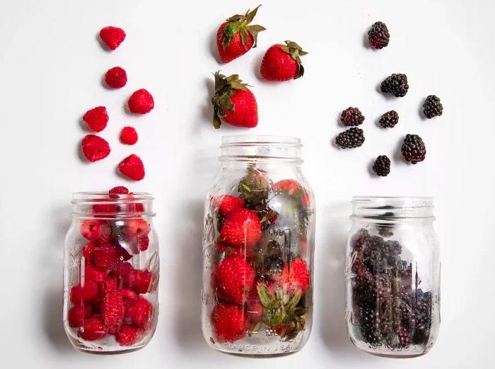 Raspberries, strawberries, and blackberries spilling out of mason jars, photographed after one week of refrigeration.