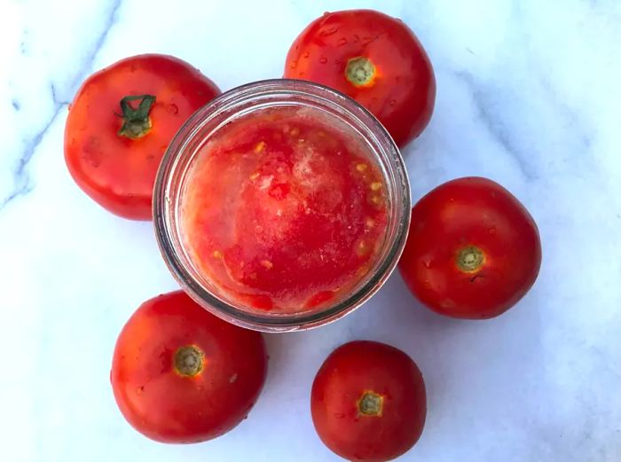 a jar filled with frozen tomatoes surrounded by fresh whole tomatoes