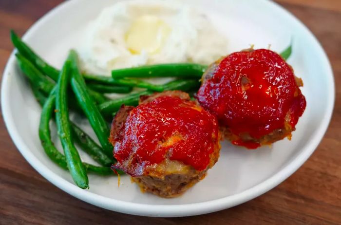 Two mini meatloaves served with green beans and mashed potatoes on a plate.