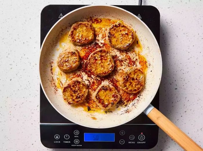 A large skillet filled with browned Italian sausage patties