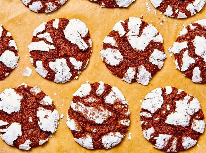 A close-up, overhead view of several chocolate crinkle cookies resting on craft-colored parchment paper.