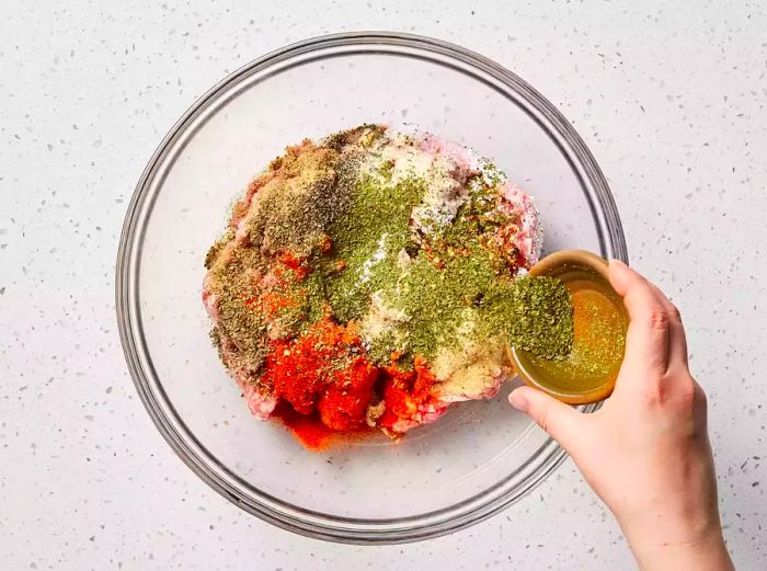 A large glass bowl filled with ground pork and various spices sprinkled on top