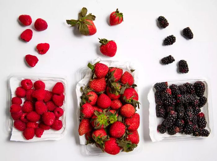 Raspberries, strawberries, and blackberries spilling out of paper towel-lined plastic containers, after one week in the fridge.