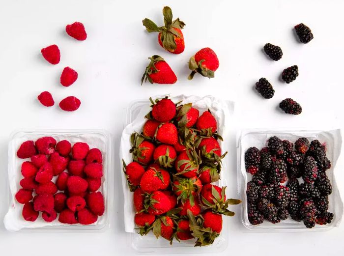 Raspberries, strawberries, and blackberries spilling out of paper towel-lined plastic clamshells, photographed after two weeks in the fridge.