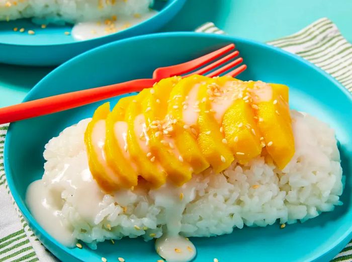 A dish of Thai sweet sticky rice topped with mango slices, drizzled with extra sauce, and sprinkled with sesame seeds