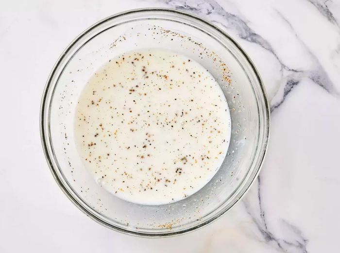 A bowl containing a mixture of buttermilk, water, salt, and pepper.